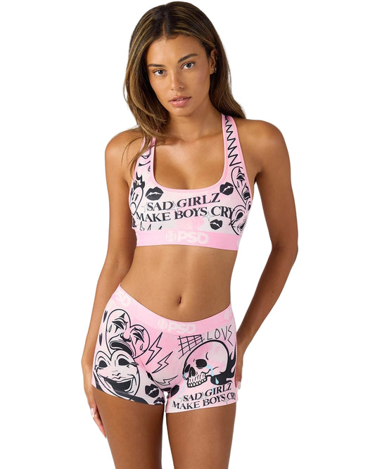 Woman wearing a pink sports bra and shorts set with graphic designs and text.